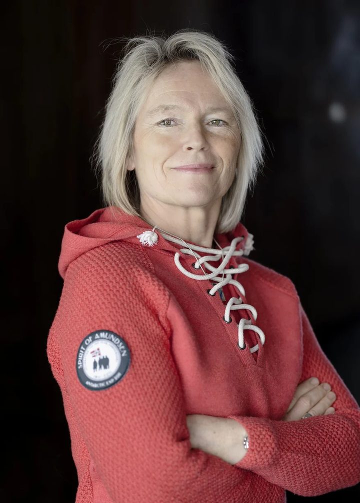 Portrait of Hilde Fålun Strøm in a red knitted sweater, smiling with her arms crossed